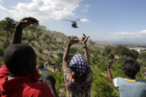 People gestures as a U.S. helicopter makes a water drop near a country club used as a forward operating base for the U.S. 82nd Airborne Division in Port-au-Prince, Haiti, Saturday, Jan. 16, 2010.  Relief groups and officials are focused on moving aid flowing into Haiti to survivors of the powerful earthquake that hit the country on Tuesday. (AP Photo/Jae C. Hong) XJH108